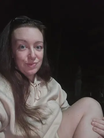 Smiling woman in a cream hoodie relaxing outdoors at night.