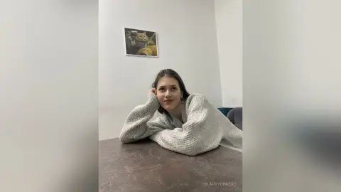 Young woman in a cozy grey knit sweater relaxing at a table in a minimalist room.