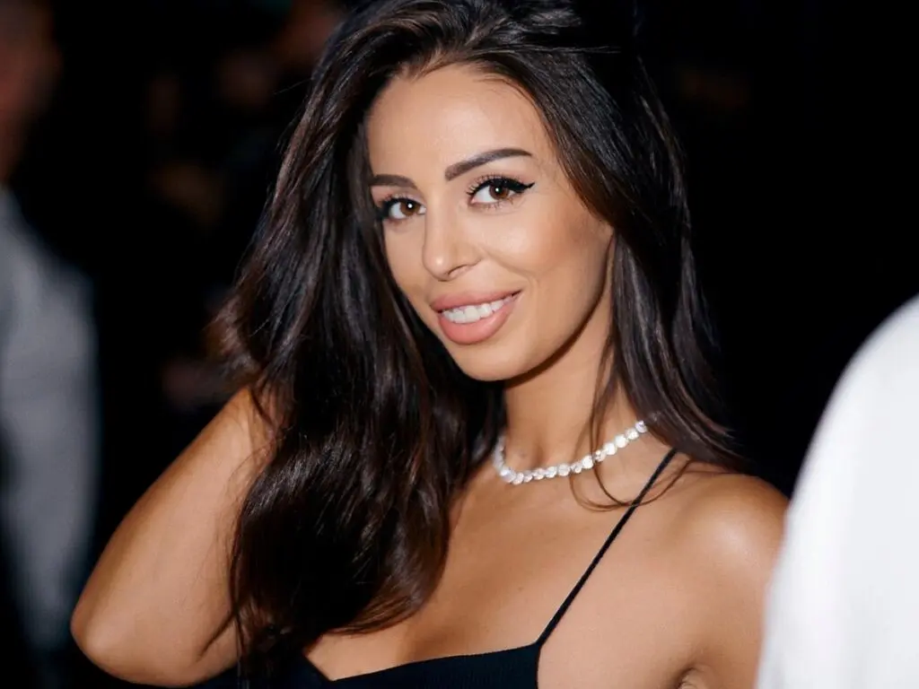Smiling brunette woman in a black spaghetti strap top at a glamorous evening event.
