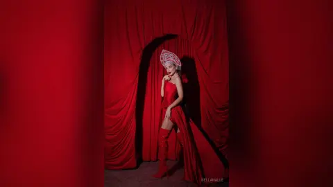 Elegant woman in a red strapless gown and ornate silver headpiece posing against dramatic red velvet curtains.