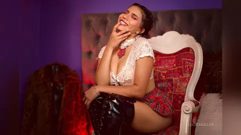 Smiling woman in white lace crop top and plaid skirt sitting on a vintage red chair in a moody purple room.