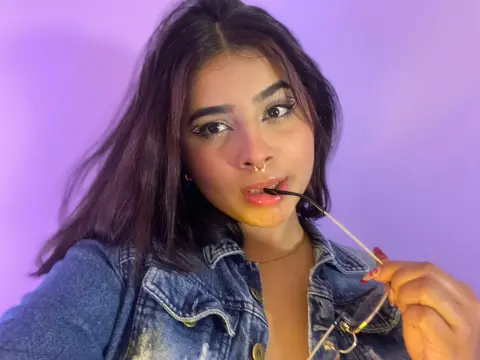 Young woman with long dark hair and nose ring wearing a denim jacket against a purple background.