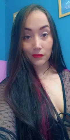 Young woman with long dark hair wearing a black lace top in a blue room with a serene expression.