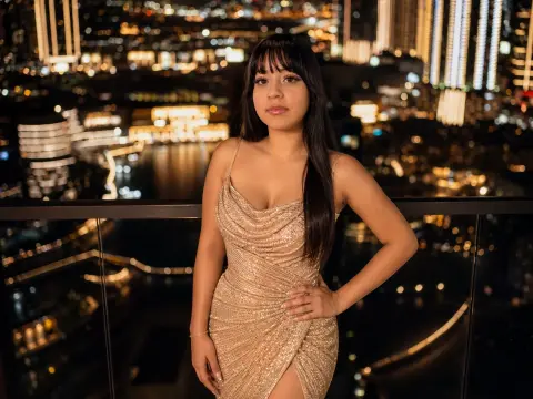 Glamorous woman in a sparkling gold sequin dress posing on a balcony overlooking a glowing city skyline at night.