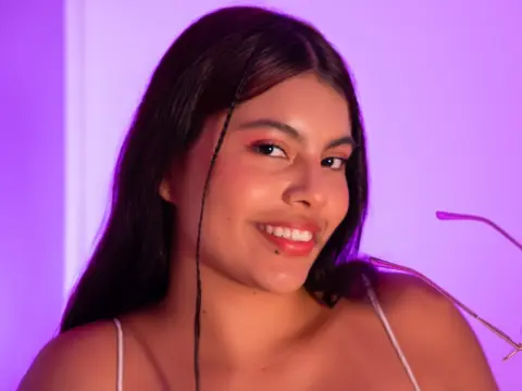 Smiling young woman with long dark hair in a white strap top against a soft purple aesthetic background.