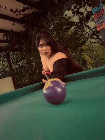 Young woman in a black off-the-shoulder top playing pool at an outdoor garden lounge.