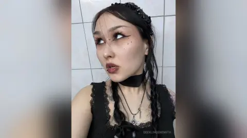 Goth woman with dark makeup and black lace outfit posing in a bathroom with a moody aesthetic.