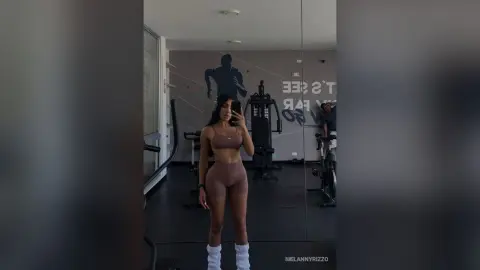Fit woman in brown seamless gym set taking a mirror selfie in a modern fitness studio.