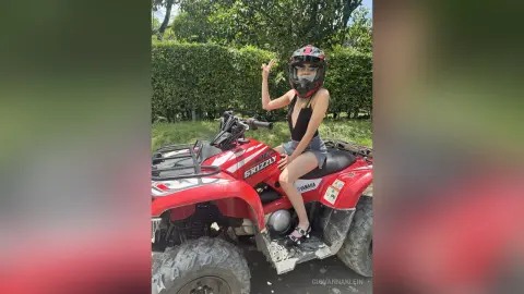 Young woman in a black tank top sitting on a red Yamaha Grizzly ATV in a lush green outdoor setting.