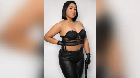 KimRoberth poses in black lace lingerie and black leather pants, wearing black gloves against a white background.