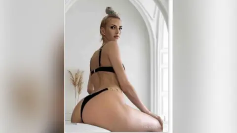 Blonde woman in black bikini posing in a bright, minimalist white room with a serene mood.