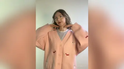 Young woman wearing a cozy pink oversized cardigan with red dachshund patterns in a bright indoor setting.