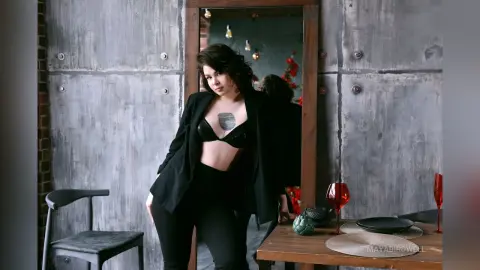Confident woman in a black blazer and bra top posing in a rustic industrial loft setting.