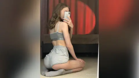 Young woman in grey loungewear taking a mirror selfie in a cozy bedroom setting.