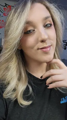 Smiling blonde woman in a black t-shirt posing for a close-up portrait in a soft-lit indoor setting.