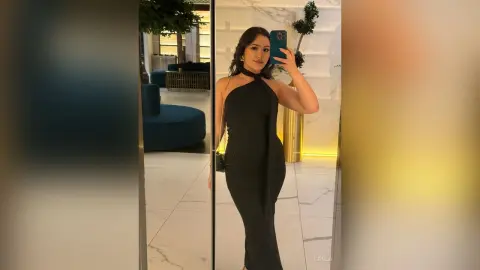 Elegant woman in a sleek black halter maxi dress taking a mirror selfie in a modern luxury living room.