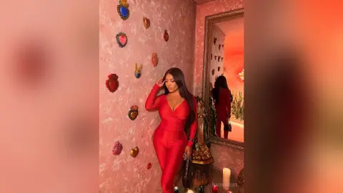 Stylish woman in a red jumpsuit posing in a romantic room decorated with heart-shaped wall art.
