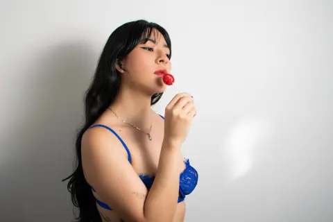 Susanmaeda is a woman with long black hair wearing a blue lace bra while holding a red lollipop to her lips.