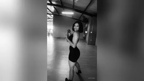 Smiling woman in a black mini dress taking a mirror selfie in a spacious, modern studio setting.