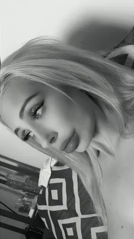 Close-up portrait of a blonde woman in a patterned top with a soft, moody aesthetic.