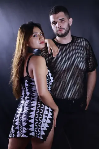 Stylish couple in edgy black mesh and sequin outfits posing against a dark studio background.