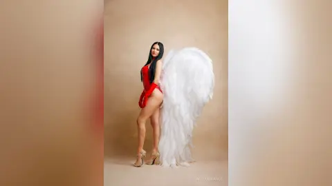 Elegant woman in a red bodysuit with large white angel wings posing against a neutral studio background.