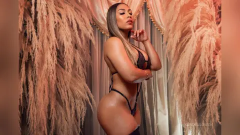 Glamorous woman in black lingerie posing against elegant beige pampas grass decor in a warm, moody setting.