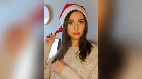 Young woman in a cozy white sweater and red Santa hat smiling in a bright indoor setting.