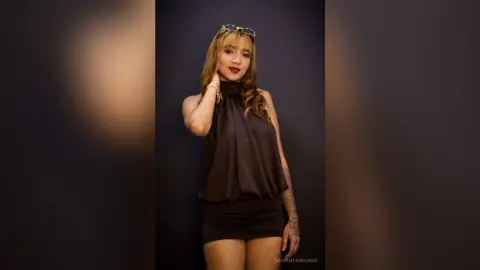 Stylish woman in a black halter neck top and mini skirt posing confidently against a dark studio background.