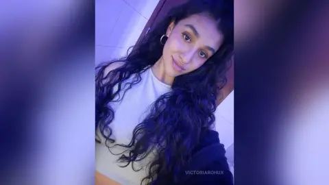 Young woman with long wavy hair wearing a white tank top in soft blue moody lighting.