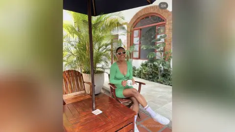 MissyJohansson smiles wearing a green dress and sunglasses while sitting at an outdoor table with a white mug.
