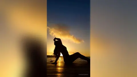 Silhouette of a woman relaxing on a wooden pier during a golden sunset over the ocean.