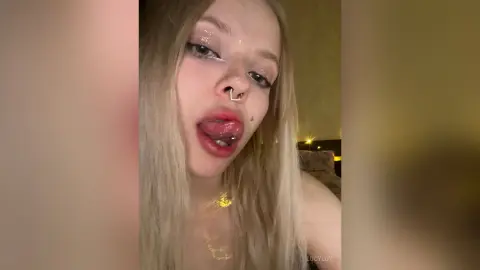 LucyLoy with blonde hair and glittery eye makeup sticks her tongue out at the camera.