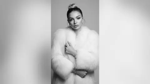 Elegant woman in a white faux fur coat posing against a studio background in a sophisticated black and white portrait.