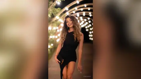 Glamorous woman in a chic black cocktail dress posing under glowing fairy lights at a night event.