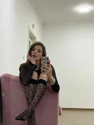 Young woman in a black long-sleeve top and leopard print tights taking a mirror selfie on a pink velvet sofa.