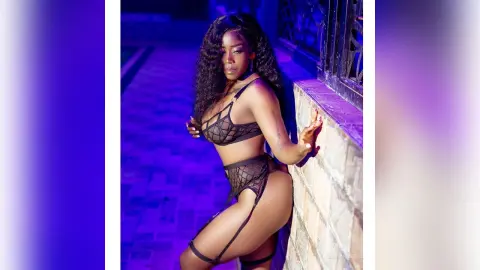 Glamorous woman in black lace lingerie posing in moody blue nightclub lighting.