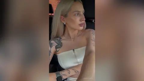 LowerFrancis, a blonde woman with tattoos on her shoulder and arm, wearing a white strapless zip-up top and a silver necklace.