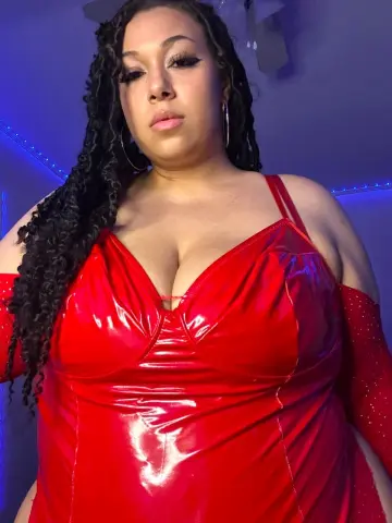 Curvy woman in a glamorous red latex dress with long braids posing under blue mood lighting.