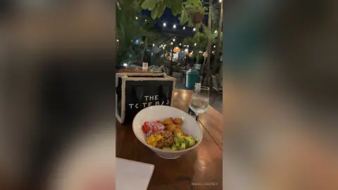Healthy grain bowl with avocado and vegetables served on a wooden table at an outdoor evening cafe.