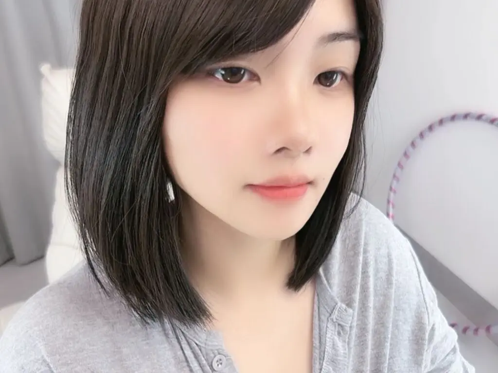 Close-up portrait of a young woman with short dark hair wearing a grey shirt in a bright indoor setting.