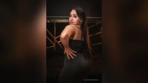Young woman in a sleek black strapless dress posing confidently in a dark studio setting.