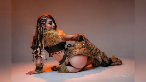 Woman in tribal barbarian cosplay with faux fur outfit and braided hair sitting in a studio setting.