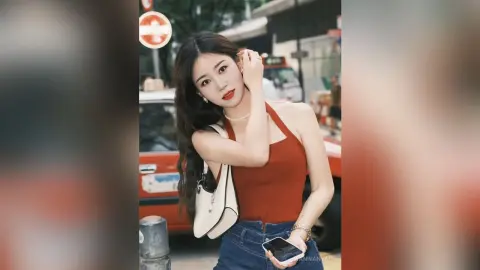 Young woman in a burnt orange halter top and jeans posing on a city street with a white handbag.