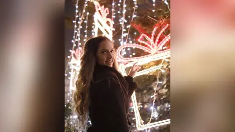 TiffanyAddams smiles while standing outdoors at night, wearing a black jacket with her long brown hair flowing down her back.