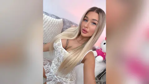 Blonde woman in a white lace dress relaxing on a bed with a dreamy, soft aesthetic.