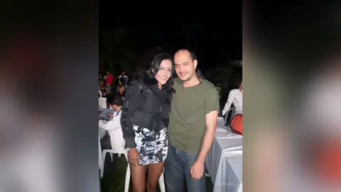 Smiling man in olive t-shirt and woman in black top posing together at an outdoor evening event.