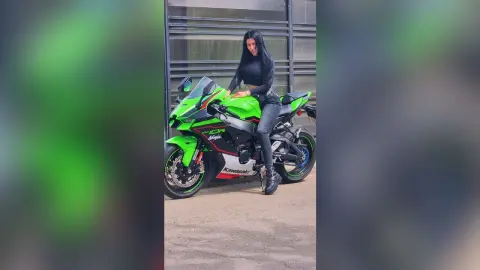 Stylish woman in black outfit posing confidently on a green Kawasaki Ninja motorcycle in an urban setting.