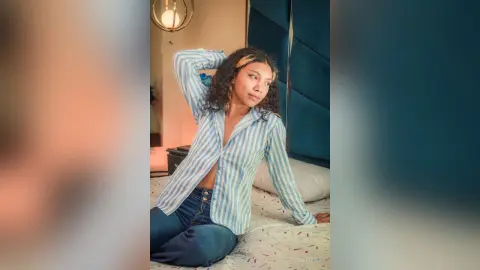 Young woman in a blue striped button-down shirt relaxing on a bed in a cozy, sunlit bedroom.