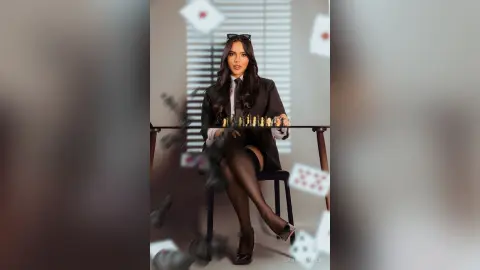 Elegant woman in a black blazer and tights sitting at a desk in a moody, cinematic office setting.